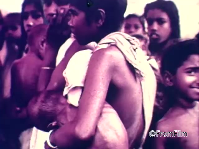 The still from the 'CARE World Hunger Fund PSA - 1975' depicts a group of individuals, predominantly children, in a poignant moment highlighting the effects of hunger. A child is being held close, with emaciated features visible. The expressions of those in the background convey concern and distress, emphasizing the urgent need for humanitarian aid. The imagery evokes empathy and awareness regarding the global hunger crisis.