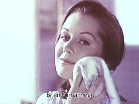 The still from the 1968 Ivory Soap commercial features a woman smiling softy while gently using a washcloth to cleanse her face. The image conveys a sense of freshness and cleanliness, typical of soap advertisements of that era. The warm, nostalgic color palette adds to the classic feel of the commercial.
