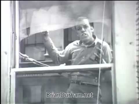 The still from 'Clean Air PSA - 1968' depicts a man leaning out of a window, likely addressing the audience about air quality issues. He appears distressed, conveying a sense of urgency regarding the importance of clean air. The grayscale aesthetic emphasizes the seriousness of the message. It captures a moment emphasizing the human impact of environmental concerns.