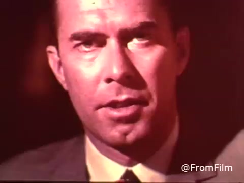 The still from the 1970s Colgate Toothpaste commercial features a man in a suit, showcasing a serious expression. The image is warm-toned, characteristic of 16mm film, and captures a moment that likely emphasizes the benefits of MFP fluoride in Colgate toothpaste. The focus on the man's face suggests a direct appeal to the audience, typical of advertising in that era.