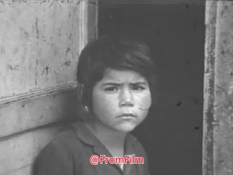 The still from the 1968 PSA 'Trick or Treat for UNICEF' features a young child looking somberly out from a doorway. Accompanying the visual is a voiceover highlighting the impact of UNICEF’s efforts, noting that children in over a hundred countries will benefit from health and happiness due to the collective actions of millions. The context emphasizes the importance of children's involvement in helping others through the Halloween campaign.