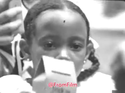 The still from the 1968 PSA 'Trick or Treat for UNICEF' features a young girl with braids, holding a UNICEF donation box. The background suggests a festive setting, likely during Halloween. The voiceover emphasizes the positive impact of children's efforts in raising funds to help other children worldwide. The song 'Some Day My Prince Will Come' juxtaposes the theme of hope and helping others.