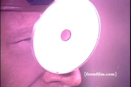 The still from the 'Schick Super II' commercial features a close-up of a man's face, focusing on his eye and the razor blade. The blade is positioned in front of his eye, creating a stark visual juxtaposition. The image is somewhat washed out, typical of 16mm film prints from the 1970s, with a slight purple tint. This dramatic angle emphasizes the precision and sharpness of the product being advertised.