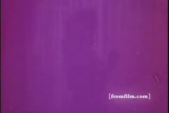 The still from 'Glade Air Freshener - 1970's' features a predominantly purple background, likely due to the aging of the 16mm print. A silhouette or shadowy figure is faintly visible, suggesting movement or interaction within the scene. The image conveys a sense of nostalgia, characteristic of advertisements from that era, with a focus on vibrant colors and simple visuals.