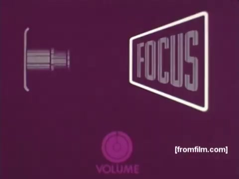 The still from 'IBM: Once Upon A Punched Card' (1964) features a vintage design, showcasing a projector lens beside a large 'FOCUS' graphic on a purple background. Below, an indicator for 'VOLUME' adds to the retro aesthetic. This imagery reflects the film's exploration of the evolution of punch cards in computing, connecting early technology to its 1964 context. Follow us on Twitter @FromFilm for more insights!