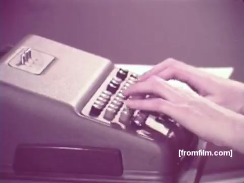The still from 'IBM: Once Upon A Punched Card (1964)' features a close-up of a person's hands typing on a classic punch card machine. The machine, with its vintage design, highlights the era's technology, emphasizing the tactile and manual process of data entry. The film captures the significance of punch cards in computing history, showcasing their evolution up to 1964. The image reflects a nostalgic glimpse into the past of computing practices.   Follow us on Twitter @FromFilm.