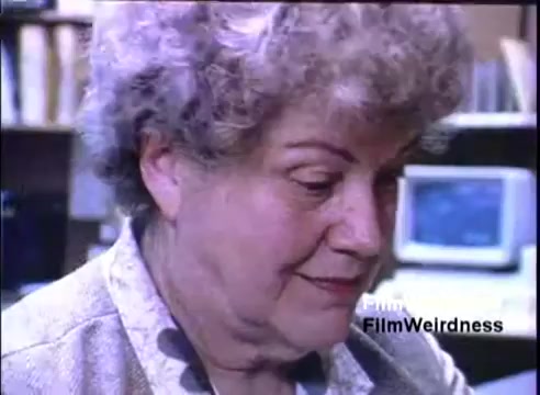 The still features a woman with curly hair, looking intently at something off-screen. She appears to be in a professional or office environment, with a computer visible in the background. The context is tied to the IBM System 36 sales film from 1984, likely showcasing real-life applications of the technology.