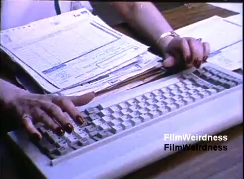 The still features a close-up of a hands typing on a keyboard, set against a cluttered desk with papers and documents. It showcases 1980s office technology, emphasizing the IBM System 36's role in business environments. The aesthetic conveys a professional atmosphere from that era.