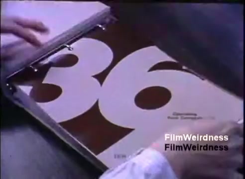 The still features a hand flipping open a binder to reveal a prominently displayed page with the number '36' in large, bold typography. The design emphasizes the IBM System 36, likely part of a presentation or promotional material. The background is subdued, focusing attention on the binder's content. The overall aesthetic reflects the corporate style of the early 1980s, typical for sales materials of that era.