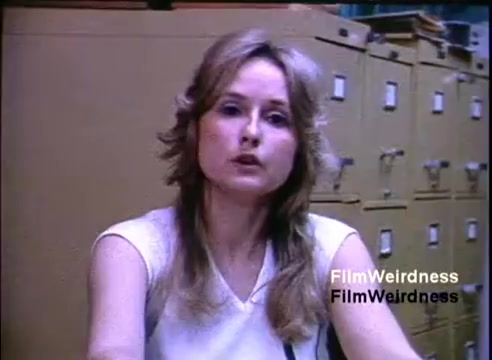 The still features a woman with long, light-colored hair, speaking directly to the camera. She is seated in front of filing cabinets, suggesting an office environment. Her expression appears serious, as though she is discussing details related to the IBM System 36. The overall aesthetic reflects the style of promotional films from the 1980s.