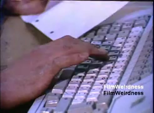 The still features a close-up shot of a hand typing on a keyboard, likely from the early 1980s, as part of the IBM System 36 sales film. The keyboard appears to have an older design, common during that era, with distinct, large keys. A sheet of paper is partially visible, suggesting the context may involve data entry or document preparation related to the IBM System 36. The focus is on the hand and keyboard, emphasizing the action of typing.