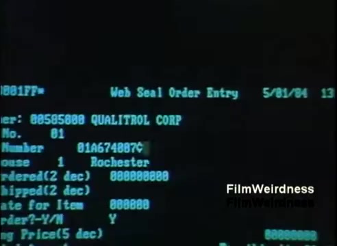 The still features a screen displaying a computer interface, likely from an IBM System 36 in 1984. It shows order entry details, including a customer name ('QUALITROL CORP'), order number, location ('Rochester'), and various fields for item details. The interface has a green text on a black background typical of that era's computing, emphasizing a straightforward data input layout. The date displayed is May 1, 1984.