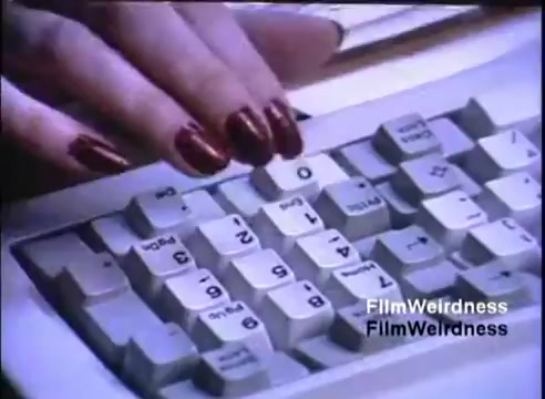 The still features a close-up of a female hand with long, manicured red nails typing on a computer keyboard. The keyboard appears to be from the IBM System 36, showcasing several numeric and function keys. The lighting creates a focused effect on the hand and fingers, emphasizing the act of typing.
