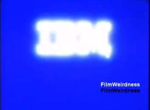 The still features the IBM logo prominently displayed in a blurred, glowing white against a bright blue background. The focus on the logo emphasizes its brand identity, typical of promotional materials. The overall aesthetic reflects the design trends of the 1980s, aiming to capture viewer attention with vibrant colors and bold graphics.