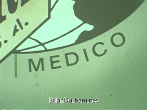 The still from the 'Medico CARE PSA - 1960s' features a close-up of a logo or emblem, prominently displaying the word 'MEDICO.' The color palette has a faded, vintage look typical of 16mm film from that era, likely conveying a sense of health awareness or medical outreach associated with public service announcements. The overall composition emphasizes the importance of medical care.