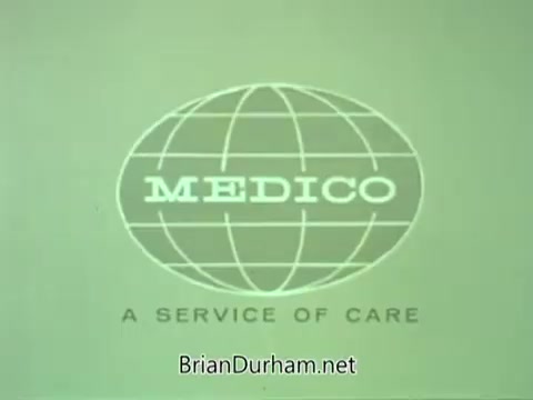 The still features a logo for 'MEDICO,' which is presented within a globe outline. The text reads 'MEDICO' prominently, with a subtitle stating 'A SERVICE OF CARE.' The background is a muted green, giving it a vintage feel typical of the 1960s era. This image is indicative of a public service announcement (PSA) promoting health care services.