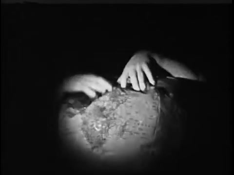 The still features a close-up of hands interacting with a globe, conveying a sense of exploration or concern for global issues. The lighting is low, creating a somber tone, which aligns with the theme of the 1967 Save the Children commercial, emphasizing the importance of awareness and action regarding children's needs worldwide.