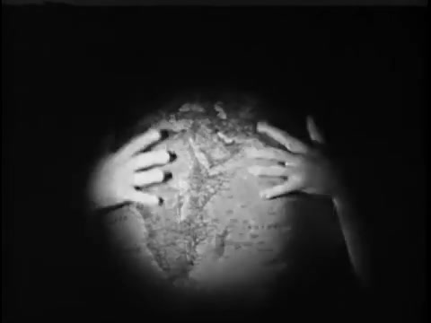 The still depicts a pair of hands reaching out towards a globe, emphasizing a global perspective. The image is likely shot in black and white, creating a dramatic and somber mood. The focus on the hands suggests a theme of care and responsibility, possibly highlighting the importance of helping children around the world as part of the Save the Children campaign.