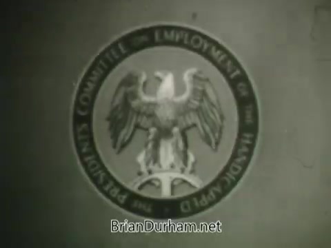 The still from the 'Hire the Handicapped' PSA features a circular emblem that symbolizes support for the employment of handicapped individuals. The design includes an eagle, representing strength and freedom, and emphasizes the importance of providing opportunities for veterans and people with disabilities. The message encourages viewers to consider their role in helping these individuals find meaningful work, promoting the idea of ability over disability. The overall tone is motivational, highlighting the potential and eagerness of those willing to contribute to the workforce.