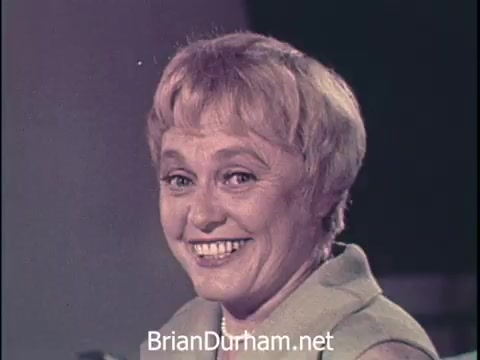 The still from the 'Oxydol laundry detergent' commercial features a smiling woman with short, wavy hair, dressed in a light-colored outfit. Her cheerful expression emphasizes the positive sentiment associated with using the product. The setting appears to be a studio environment typical of 1960s advertisements, designed to promote the efficacy of laundry detergent.