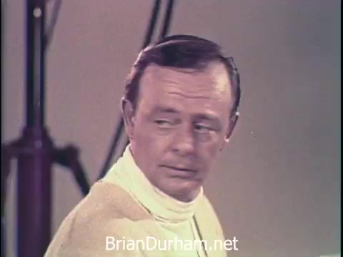 The still features a man looking away from the camera in a casual, yet slightly contemplative pose. He is dressed in light clothing, typical of the 1960s fashion. The background appears simple, likely set up for a commercial shoot, with lighting equipment partially visible. The context suggests this image is part of an advertisement for Oxydol laundry detergent, emphasizing a relatable, engaging presentation aimed at viewers.