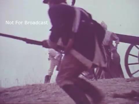 The still from the 'Molly Pitcher Bicentennial Savings Bonds PSA' depicts a scene reminiscent of military action from the American Revolutionary War. Soldiers are seen in historical attire, with one in the foreground carrying a musket, while a cannon and additional figures can be identified in the background. The overall tone is serious, reflecting themes of patriotism and sacrifice associated with the bicentennial celebration.