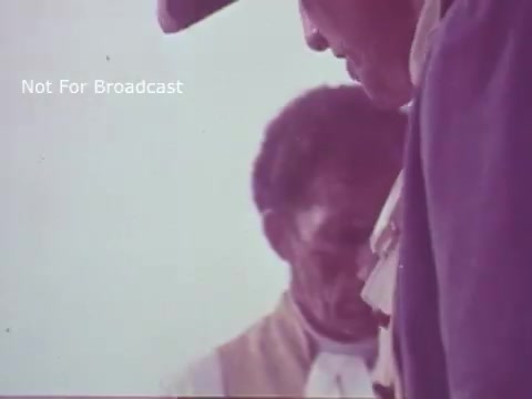 The still from the 'Molly Pitcher Bicentennial Savings Bonds PSA' features historical figures in period attire, likely representing figures from the American Revolutionary War. The focus seems to be on two individuals, one prominently in profile, engaging with each other. The color tone appears soft and faded, typical of 16mm film, evoking a sense of nostalgia. The context relates to the bicentennial celebration, highlighting themes of patriotism and investment in the future through savings bonds.