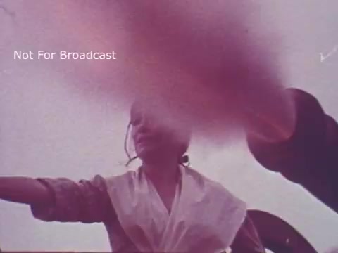 The still from the 'Molly Pitcher Bicentennial Savings Bonds PSA' features a close-up perspective of a woman in historical attire, likely representing Molly Pitcher. She appears to be engaged in a historical reenactment, possibly involved in a battle scene, as indicated by her stance and the background elements. The image is slightly obscured, adding a dynamic quality to the scene. The context ties into themes of patriotism and American history, aligning with the celebration of the bicentennial.