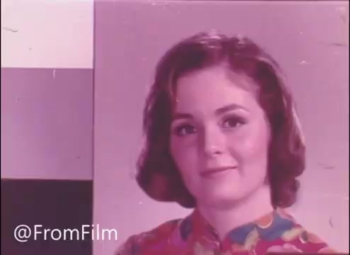 The still depicts a woman with short, wavy hair, wearing a colorful floral blouse. She has a soft, friendly expression and is looking directly at the camera. The background features a simple design, likely indicative of the 1960s or 1970s aesthetic typical in television commercials from that era. The film is labeled 'The Happy Freemans,' suggesting a lighthearted and positive theme related to the John Hancock Insurance commercial.
