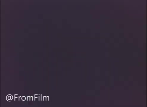 The still is a frame from a 16mm print of the TV commercial titled 'The Happy Freemans.' It features Morgan Freeman, known for his distinctive voice and presence, singing in a promotional context for John Hancock Insurance. The overall tone likely aims to convey warmth and reliability associated with the insurance brand.