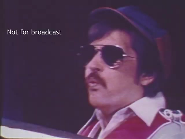 The still features a man wearing sunglasses and a cap, likely portraying a boating safety advocate or official. He has a mustache and is dressed in attire typical of the 1970s. The background suggests a staged environment, emphasizing the educational message of the PSA. The image captures the retro aesthetic of the era, resonating with the themes of boating safety and public service announcements from that time.