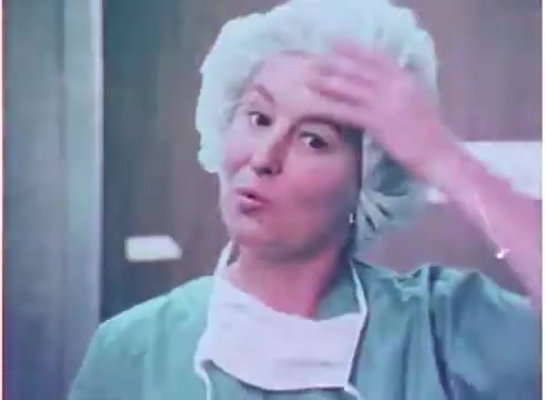 The still from the 1970s advertisement for Purolator oil filters features a woman in surgical attire, including a light blue surgical cap and mask. She appears to be in a clinical or mechanical environment, possibly a workshop or factory. The color scheme has a vintage aesthetic, typical of the 16mm film format, with soft tones and a slight graininess. The woman's expression suggests she is engaged in the demonstration or explanation of a product, conveying a sense of professionalism.
