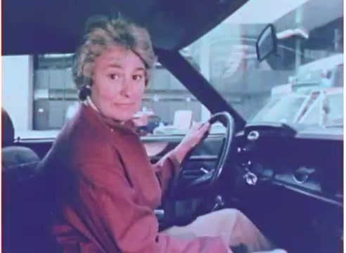 The still depicts a woman sitting in the driver's seat of a car, looking over her shoulder with a slightly surprised expression. She is dressed in a reddish-brown coat, and the interior of the car is classic for the era. The background features urban elements, suggesting a cityscape. The overall tone captures a nostalgic 1970s aesthetic, likely promoting the reliability of Purolator oil filters.