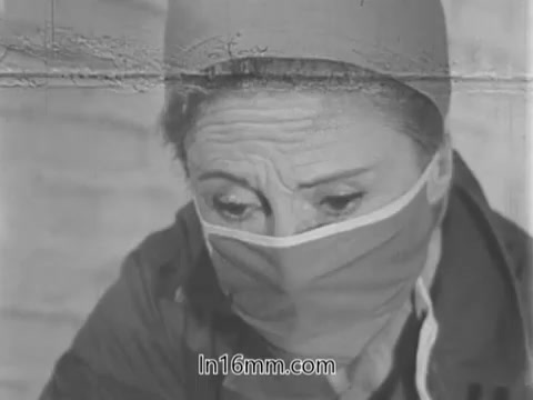 The still from the 'Guideposts Magazine PSA - Nurse - 1960s' features a nurse wearing a mask and a head covering, looking down with a serious expression. The image conveys focus and dedication, reflecting the compassionate work of healthcare professionals during that time. The aesthetic has a vintage quality, typical of 16mm film, with slight grain and wear visible, adding to its historical context.