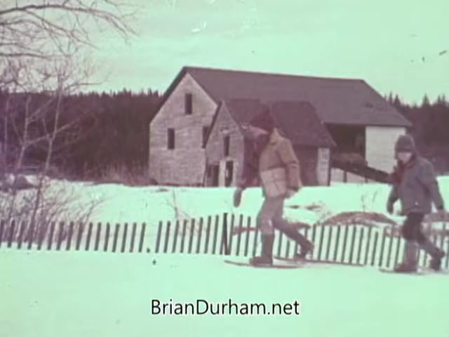 The still from the 1968 Christmas Seal PSA shows two children walking in snow, possibly on snowshoes, near a rustic stone house. A wooden picket fence is visible in the foreground, and the scene conveys a festive winter atmosphere, emphasizing themes of community and health awareness associated with the Christmas Seal campaign. The overall color tone has a nostalgic, vintage feel.