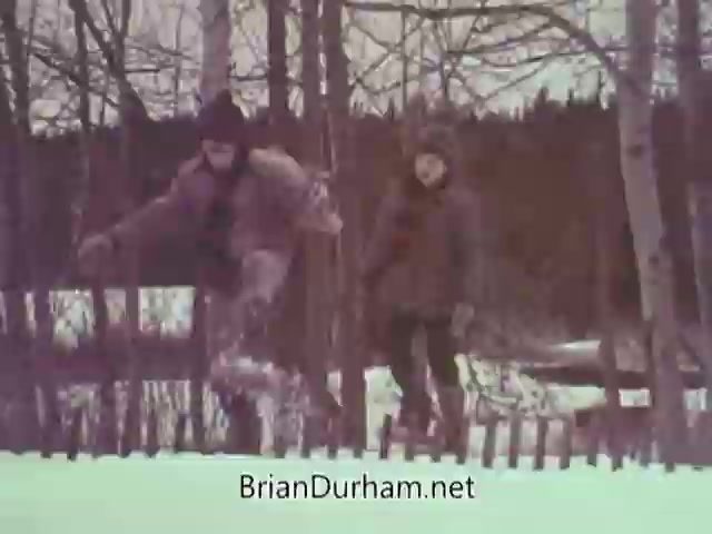 The still from the 1968 Christmas Seal PSA features two children playing in a winter landscape. One child is mid-leap over a wooden fence, while the other watches and smiles. The scene is set against a backdrop of snow and tree trunks, capturing the playful spirit of winter, likely emphasizing themes of joy and health associated with the Christmas Seal campaign.