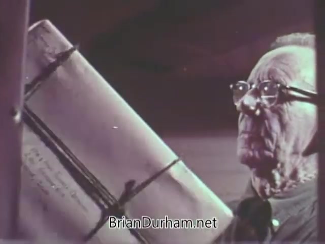 The still from the 1968 Christmas Seal PSA features an elderly man wearing glasses, holding a large, bound book or document. He appears contemplative as he gazes at the item, which is tied with string and may contain important messages or memories. The muted colors suggest a vintage aesthetic, typical of the era's film style. The scene likely conveys themes related to reflection, nostalgia, or the significance of giving during the holiday season.