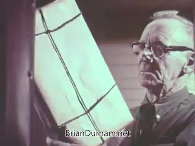 The still from the 1968 Christmas Seal PSA features an older man inspecting a large, wrapped package. He appears focused and thoughtful, wearing glasses and a simple outfit. The background suggests a homey atmosphere, likely evoking themes of holiday preparations and generosity. This scene promotes the spirit of giving associated with Christmas Seals, which fund public health initiatives.