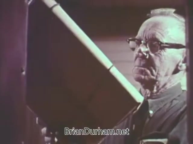 The still from the 1968 Christmas Seal PSA features an elderly man with glasses, focused intently on a task. He appears to be involved in an activity related to the holiday season, likely promoting the Christmas Seal campaign. The backdrop suggests a warm, homey environment, emphasizing themes of community and giving during the holidays.