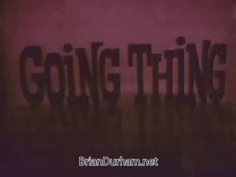 The still from the '1968 Ford Mustang Commercial' features bold, stylized text reading 'GOING THING.' The design suggests a fun, energetic vibe, aligning with the playful tone of Arte Johnson's character from 'Laugh-In.' The background appears vibrant, enhancing the promotional feel typical of 1960s advertisements, particularly for Ford’s Pop-Option sale. This commercial was aimed at the WTRF TV station in Wheeling, West Virginia, targeting local audiences.