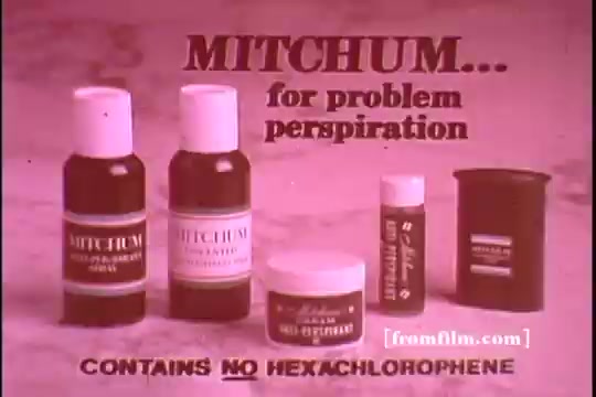 The still features a vintage advertisement for Mitchum antiperspirant products from the 1970s. It displays a lineup of various Mitchum containers, including roll-ons and sticks, prominently labeled. The text emphasizes that Mitchum is suitable for 'problem perspiration' and highlights that it 'contains no hexachlorophene.' The overall aesthetic reflects typical advertising styles of the era, with a focus on clarity and direct messaging.