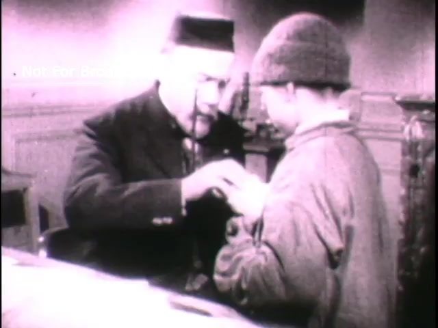 The still features a historical scene depicting Louis Pasteur in a medical setting. He appears engaged in a serious interaction with a young boy, likely demonstrating a medical procedure or administering a treatment. Pasteur, dressed in period attire, shows a focus and intent expression while the boy, dressed in a simple cap and coat, looks on with curiosity or concern. The background indicates a traditional study or lab environment, underscoring the educational theme of the PSA related to advancements in medicine and public health.