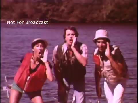 The still features three individuals on a boat near water, wearing life jackets and engaging in a lively, singing performance. The setting appears to promote boating safety, emphasizing the importance of wearing life jackets. The background suggests a natural scene, likely contributing to the message of safe boating in outdoor environments.
