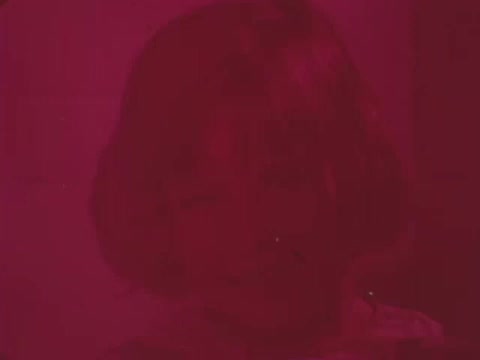 The still from the 'Easter Seals PSA - 1969' has a predominately red hue. It features a close-up of a smiling child with short hair. The overall appearance is somewhat blurred or faded, suggesting a vintage quality typical of 16mm film. The image likely conveys a positive message, consistent with Easter Seals' mission to support individuals with disabilities.