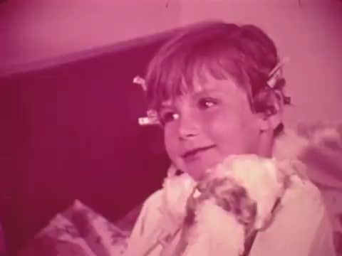 The still depicts a young boy with a cheerful expression, wearing curlers in his hair, suggestive of a playful or intimate moment. The color tones are warm, with a pinkish hue, creating a nostalgic feel. This image likely emphasizes themes of childhood and care, aligning with the message of the Easter Seals PSA, which aimed to promote awareness and support for children with disabilities.