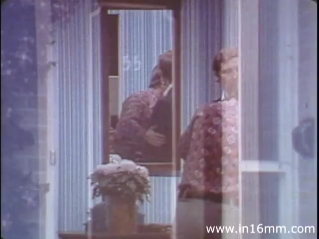 The still from 'I Am Joe's Stomach' depicts a scene where a character interacts with their surroundings, highlighted by a mirror reflecting part of the image. The setting appears domestic, featuring a striped wall and a potted plant. The use of three-dimensional animation alongside live-action sequences is indicative of the film's educational goal to illustrate the functions of the human stomach through a relatable narrative. This particular version from the 1980s likely employs visual metaphors to explore themes related to digestive health and personal experiences linked to gastrointestinal issues.