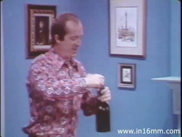 The still from 'I am Joe's Stomach' features a man in a brightly patterned shirt, standing in a well-decorated room, preparing to open a bottle. This segment illustrates the interactive and educational approach of the film, which combines live action and animation to explore the functions of the human stomach. The narrative focuses on the experiences of a character dealing with digestive issues, emphasizing the importance of caring for one's stomach and overall digestive health. The film aims to entertain while providing informative insights into bodily functions.