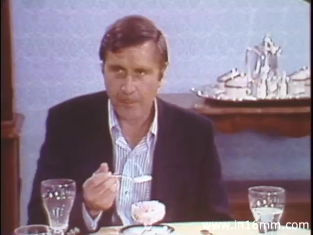 The still from 'I Am Joe's Stomach' features a man seated at a dining table, holding a spoon with a small serving of food. His expression appears thoughtful or concerned as he engages in the act of eating. The setting includes glassware and tableware that convey a domestic atmosphere. This educational film utilizes a mix of live-action sequences and animations to illustrate the complexities of stomach functions and the importance of digestive health, focusing on the character's struggles related to gastrointestinal issues.