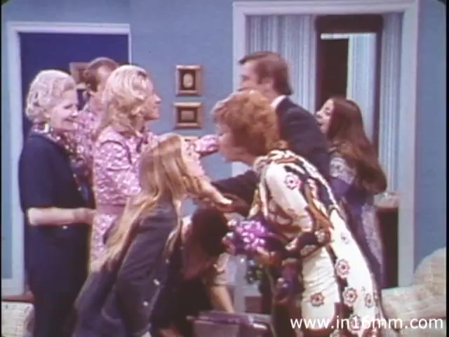 The still from 'I am Joe's Stomach' (1980s version) depicts a lively scene featuring a group of people engaged in animated social interactions. The setting appears to be a comfortable living room, characterized by a colorful and retro decor typical of that era. Various characters exhibit expressions of joy and camaraderie, suggesting a theme of connection and communication. This fits the overall narrative of the film, which combines animation and live sequences to explore the complexities of the human stomach and related health issues in a lighthearted manner.