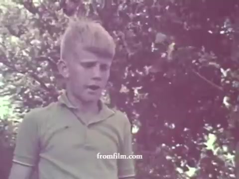 The still shows a young boy with blonde hair, wearing a light green polo shirt, standing against a backdrop of greenery. The colors are faded, typical of aged 16mm prints. The boy appears to be engaged in conversation or delivering a message related to the theme of pesticides, reflecting the educational aim of the 1967 public service announcement by the Arizona Cooperative Extension Service.